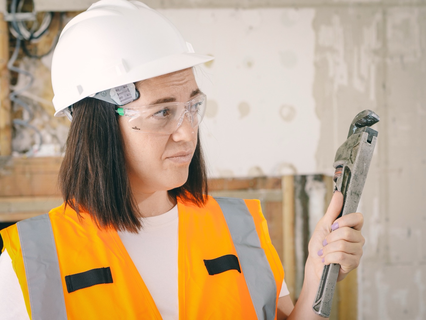 Female plumber in safety gear examining a pipe wrench on a home renovation site