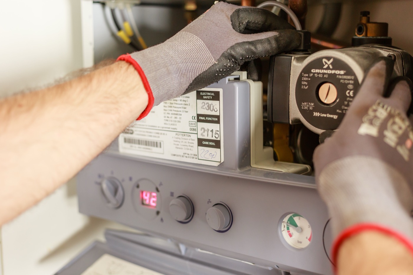 Plumber's gloved hands servicing a water heater's pump and pressure gauge before a hot water tank replacement in Abbotsford, BC